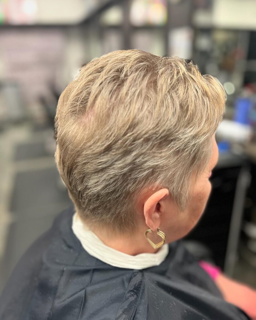 A side profile of a woman with a sandy blonde pixie cut featuring soft, brushed-back layers and short sides.