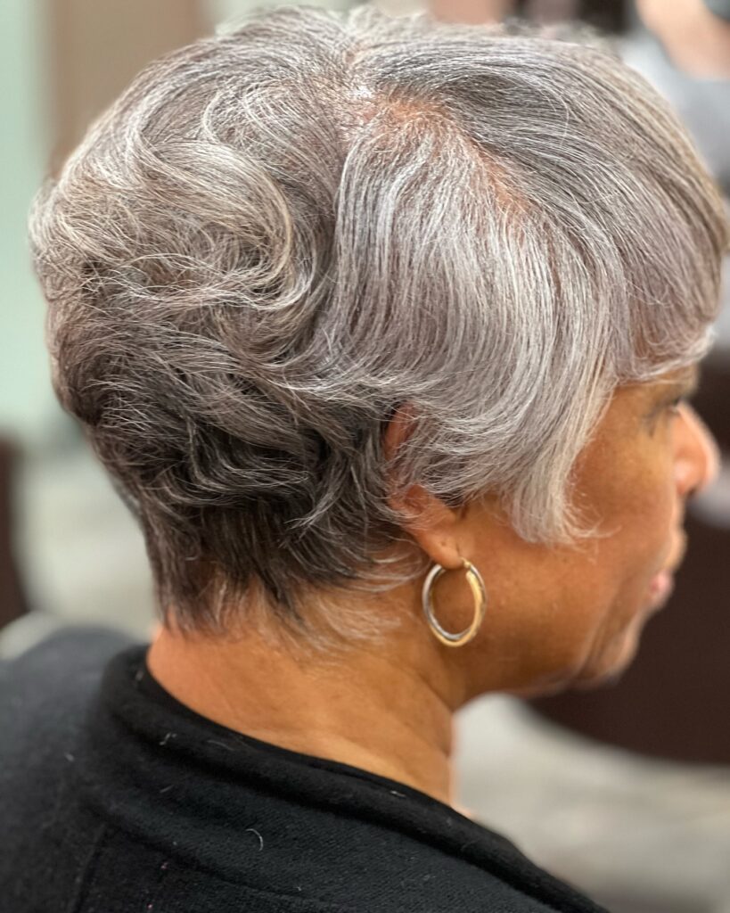 A woman with a wavy silver pixie cut featuring sculpted layers and a neat tapered neckline.
