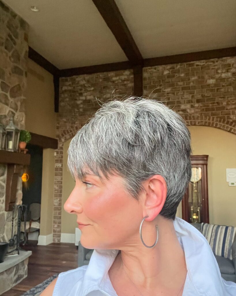 A woman with a textured salt-and-pepper pixie cut featuring short layers and a soft fringe.
