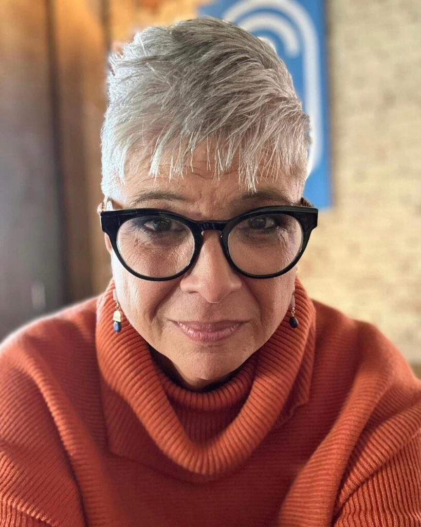 A woman over 60 with a short spiky silver pixie cut featuring dark lowlights and textured vertical layers on top.