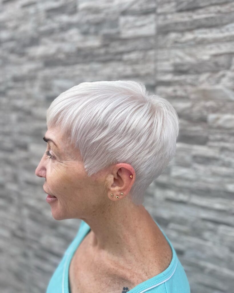 A woman in profile with a very short icy white pixie cut featuring precision layers and micro bangs.