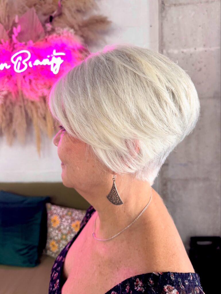 A woman over 60 with a voluminous platinum blonde wedge pixie cut featuring long layers and a tapered back.