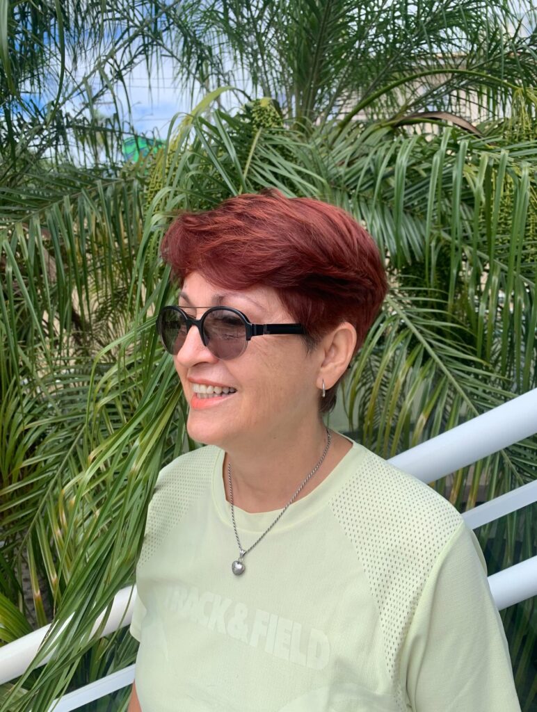 A woman over 60 with a voluminous mahogany red pixie cut featuring swept-back layers and neatly tapered sides.