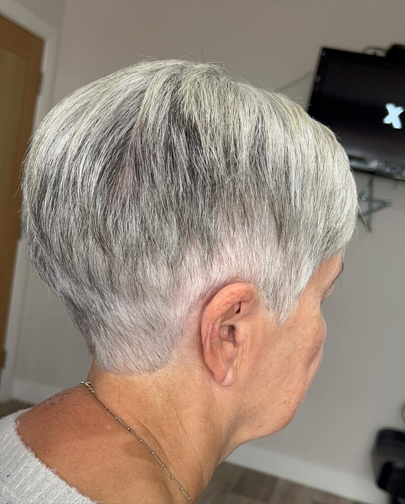 A woman in profile wearing a precision-tapered silver pixie cut with short layers and a clean neckline.