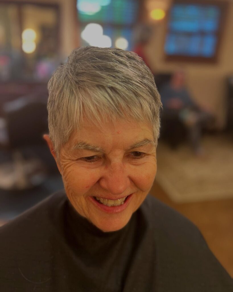 A smiling woman wearing a short charcoal and silver pixie cut with soft textured layers and a wispy fringe.