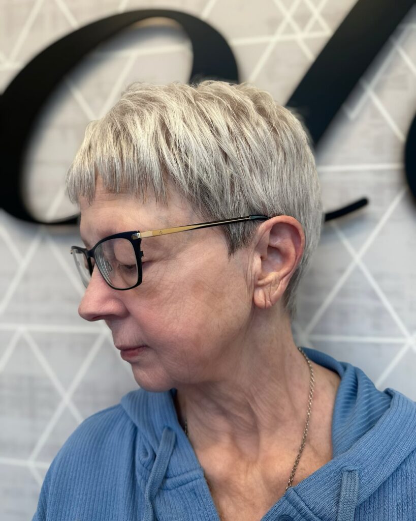 A woman in profile wearing a platinum spiky pixie cut with a choppy short fringe and dark glasses.