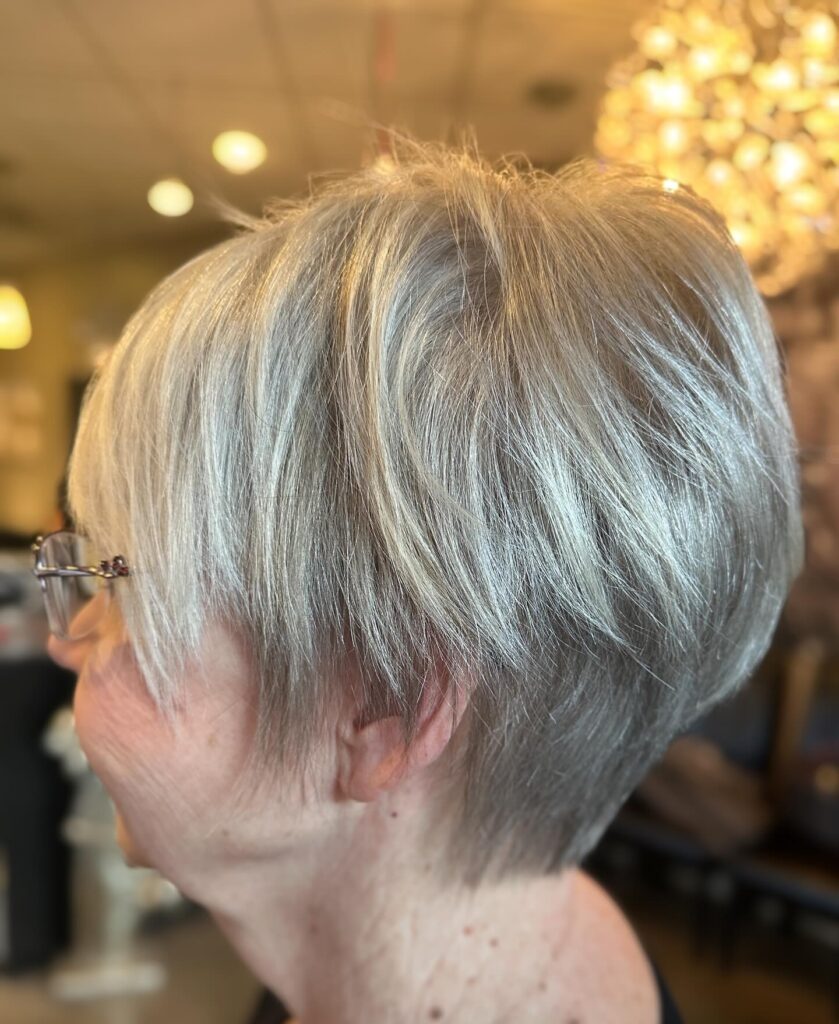 A woman over 60 with a silky champagne-silver pixie cut featuring a stacked back and soft feathered layers.