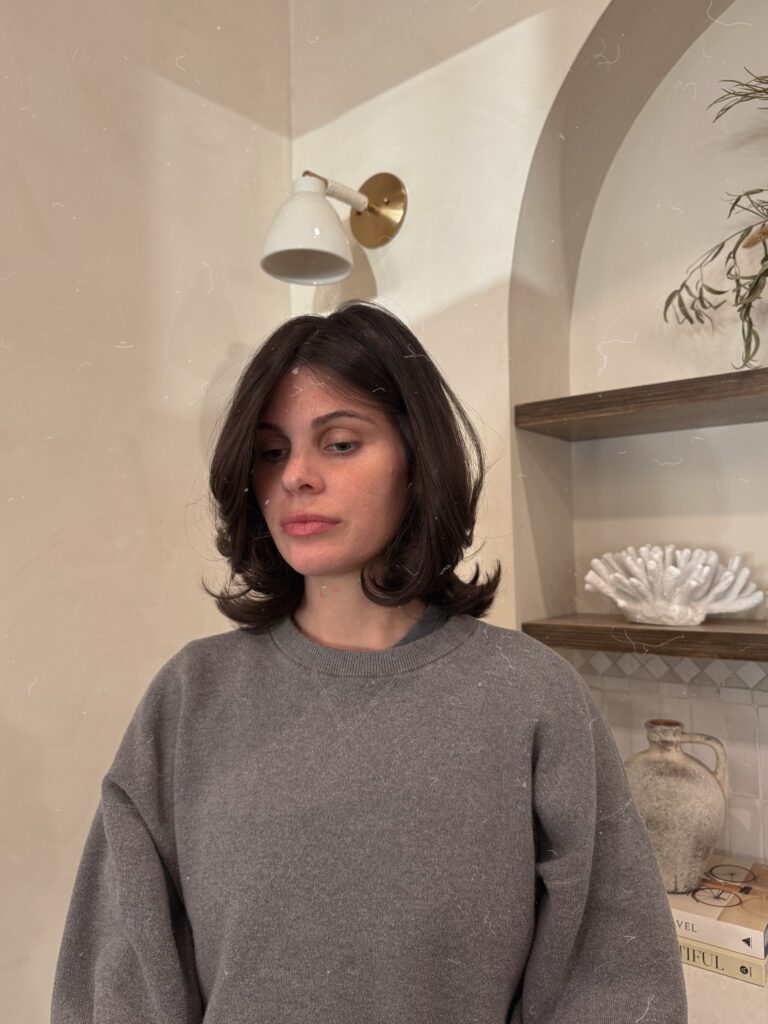A woman looking down showcasing a jaw length choppy dark brown bob hairstyle with layers that flick outward at the ends.