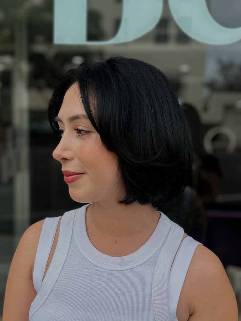 A woman smiling in side profile showcasing a jaw length choppy jet black bob hairstyle with voluminous flipped layers and a gentle lift.
