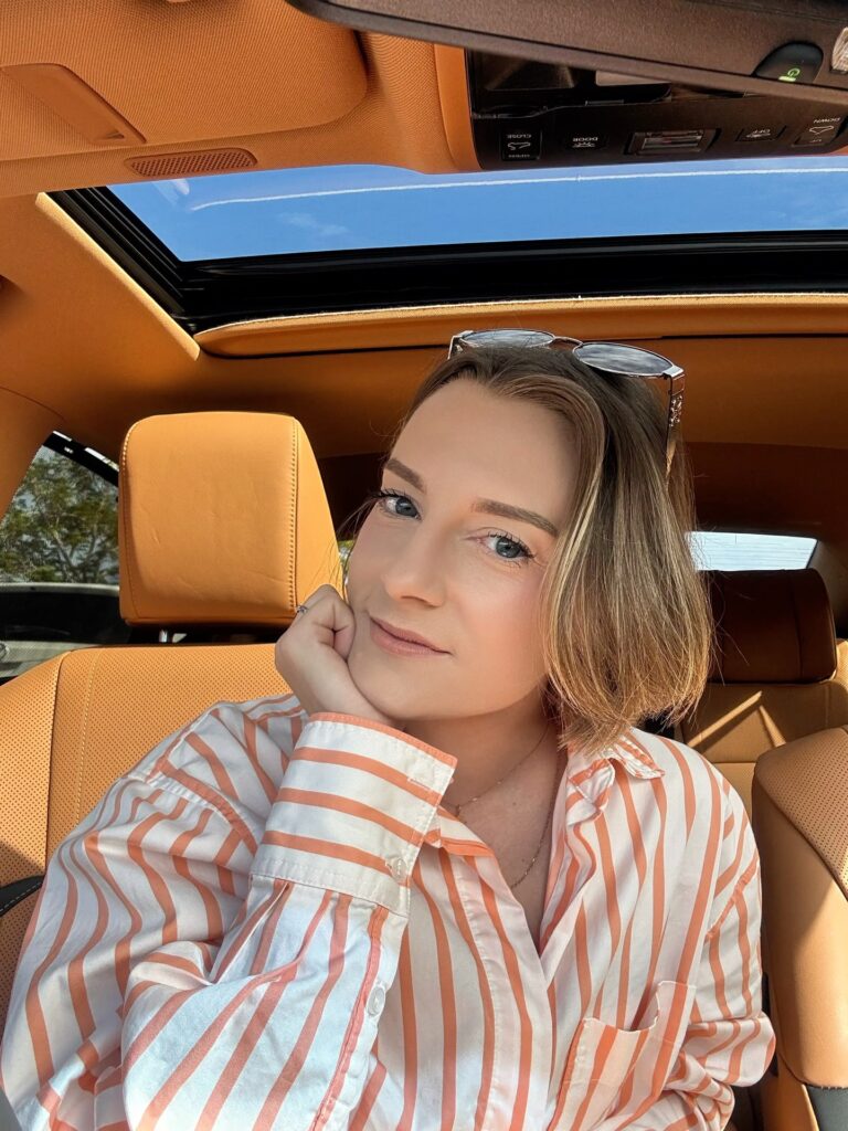 A woman smiling in a car with a jaw length choppy honey brown bob hairstyle featuring subtle highlights and a side part.