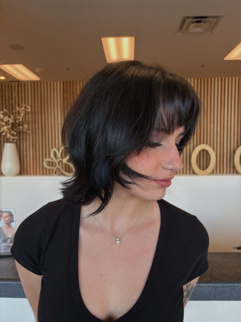 A woman with a nose ring looking down in side profile showcasing a jaw length choppy dark brunette bob hairstyle with a textured fringe and shaggy layers.