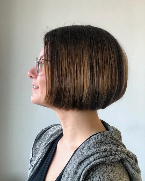 A woman viewed from the side profile showing off a jaw length brunette choppy bob hairstyle with a sleek finish and a gentle lift at the back.