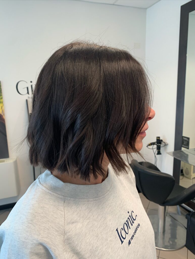 A rear view of a woman showcasing a sleek, straight dark ash blonde angled bob haircut with an ultra-clean perimeter line.