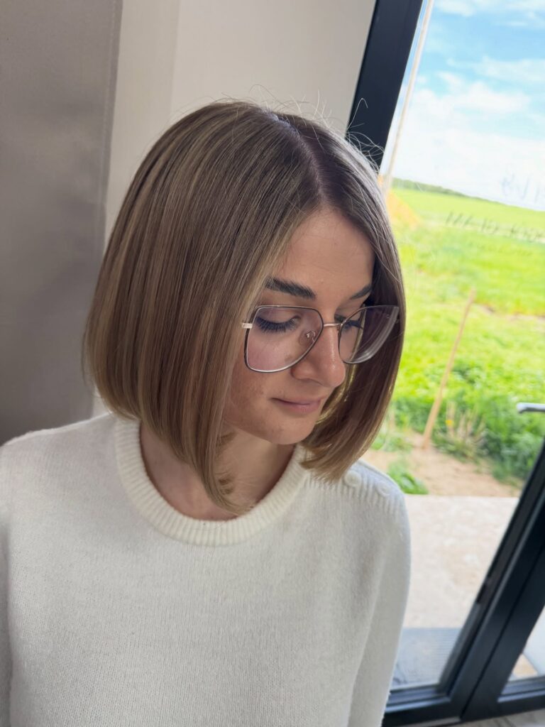 A side profile view of a woman showcasing a straight, neck-length ash blonde bob haircut with subtle internal layering and a rounded back.