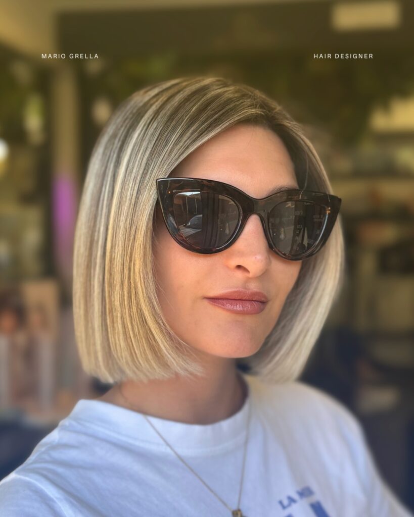 A woman wearing sunglasses showcasing a straight, collarbone-length bob haircut with high-contrast icy platinum highlights over a dark base.