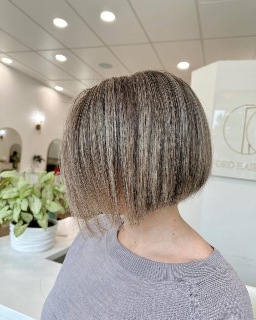 A woman with a sleek, short ash blonde angled bob haircut viewed from the side.