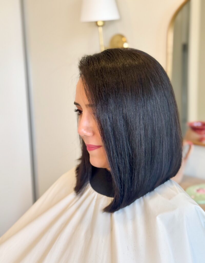 A side profile view of a woman showcasing a straight, glossy dark espresso long bob haircut with a sharp forward angle.