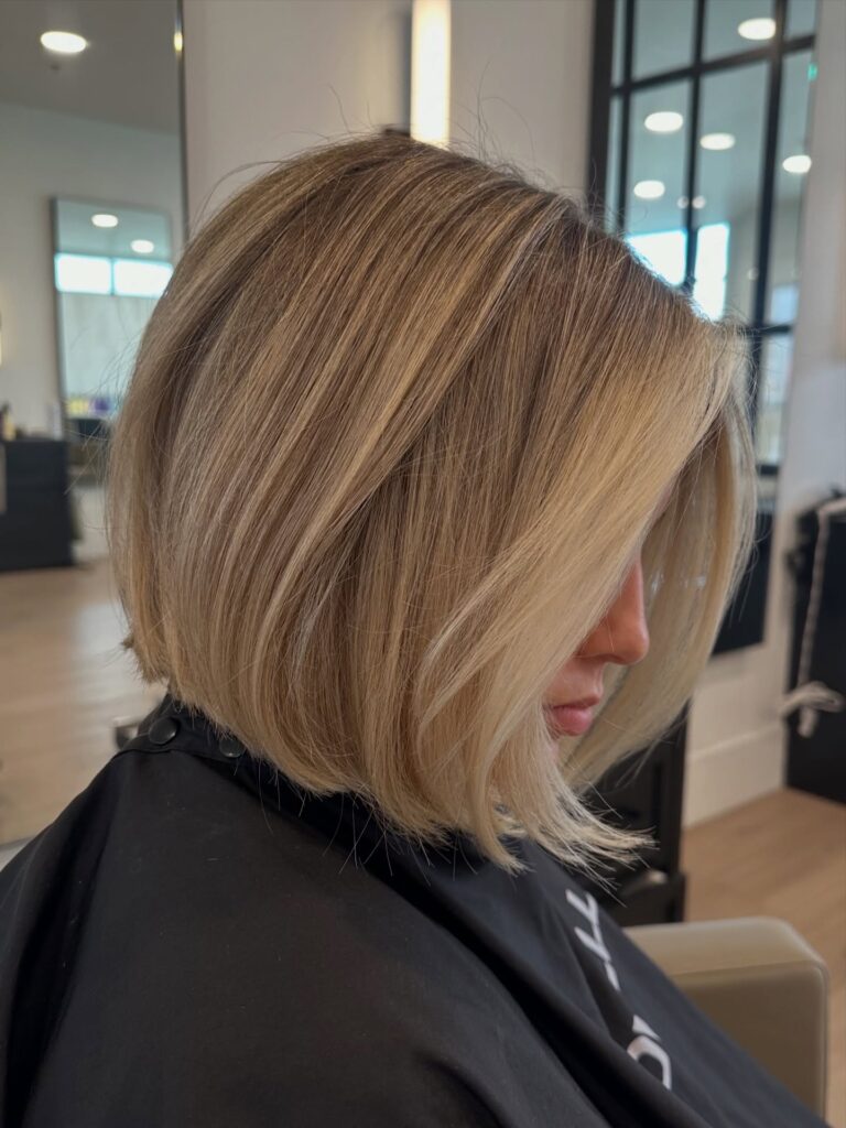 A side profile view of a woman showcasing a straight, angled vanilla blonde bob haircut with choppy ends and face-framing highlights.