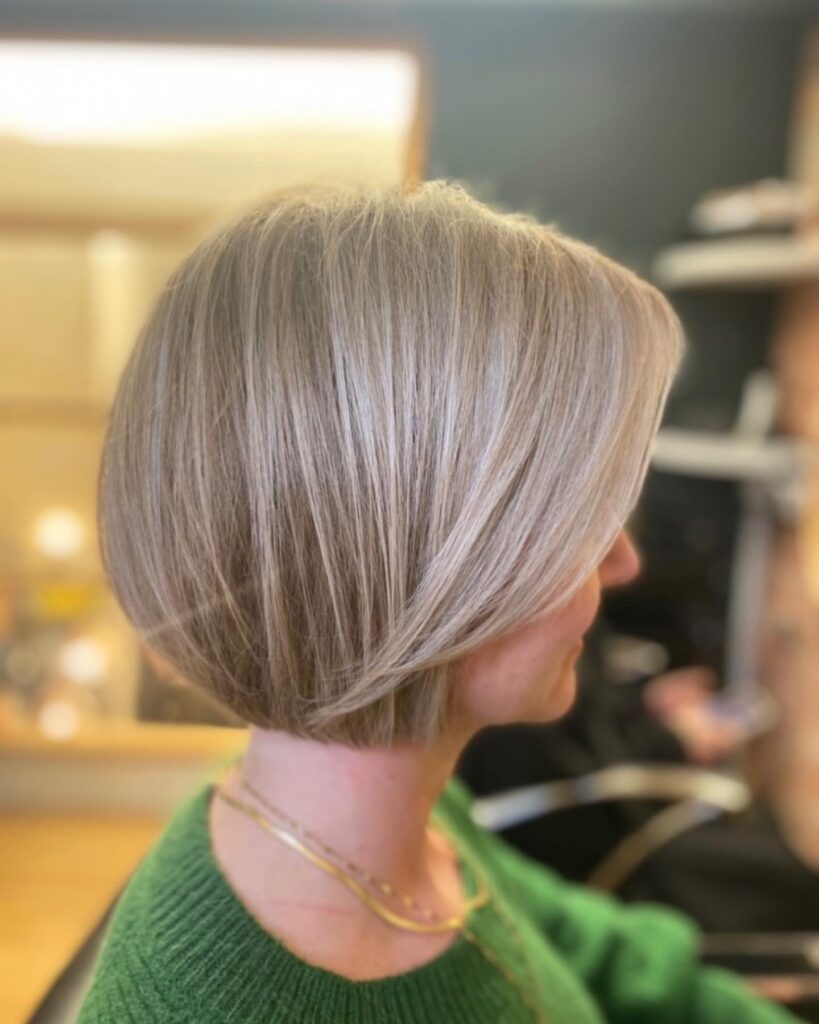 A side profile view of a woman featuring a sandy blonde stacked bob haircut with platinum highlights and a long side swept fringe.