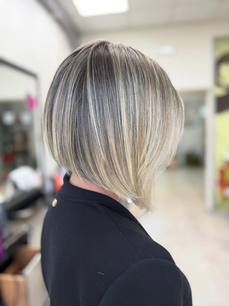 A close-up side profile view of a woman showcasing an ultra-straight, jaw-length platinum blonde angled bob haircut with sharp perimeter lines.