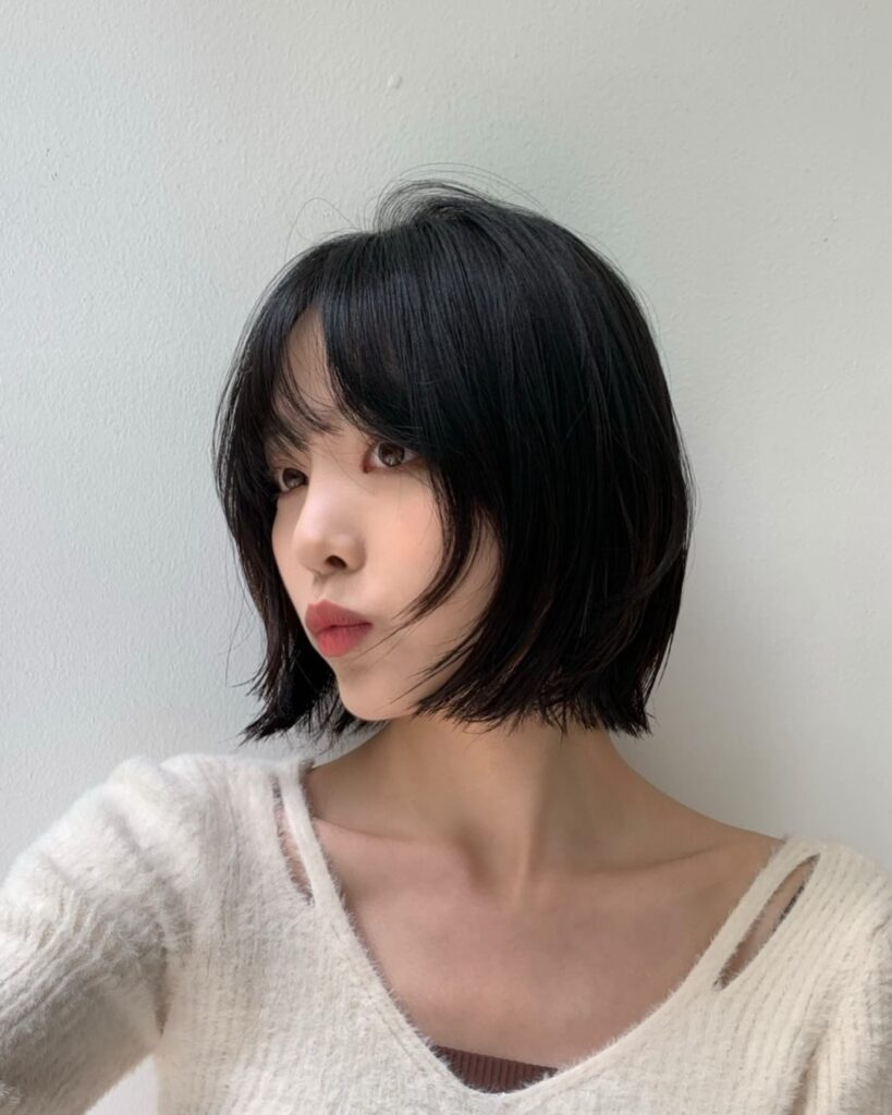Short textured layered bob with wispy bangs and soft flipped ends in glossy black hair.