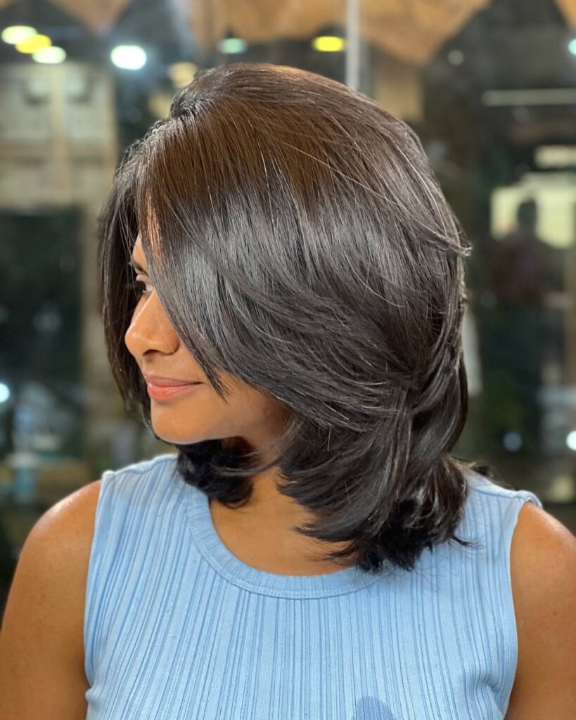 Glossy layered bob with side swept front layers and softly feathered ends in dark brunette hair.
