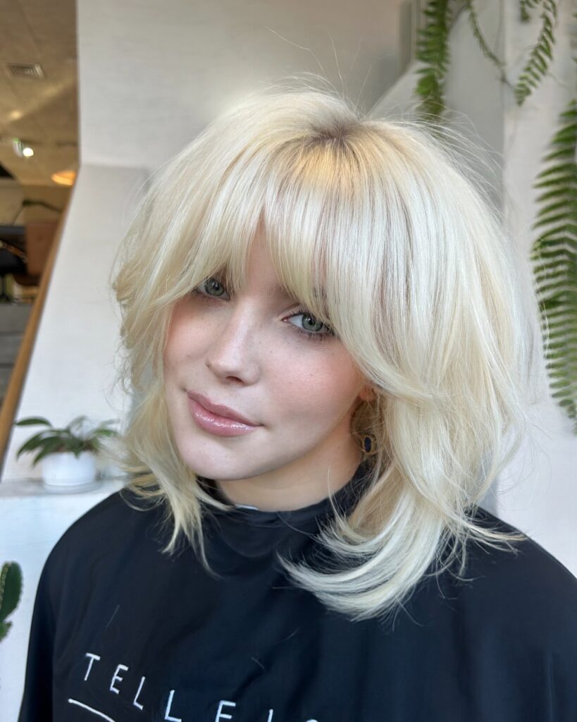 Platinum blonde layered bob with wispy curtain bangs and textured flipped ends.