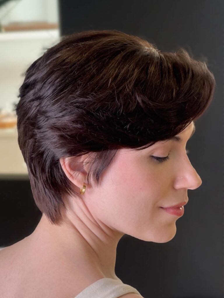 Dark brunette pixie haircut with voluminous side swept layers and a softly tapered back.