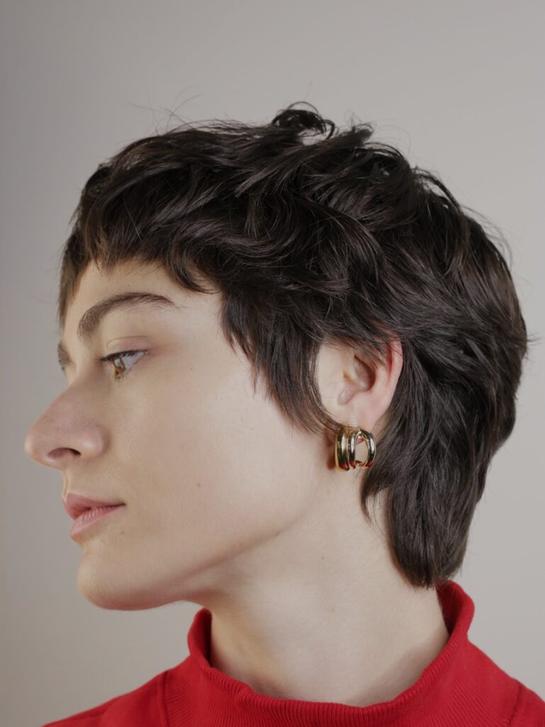 Dark brunette pixie shag haircut with tousled curly layers and soft textured movement.