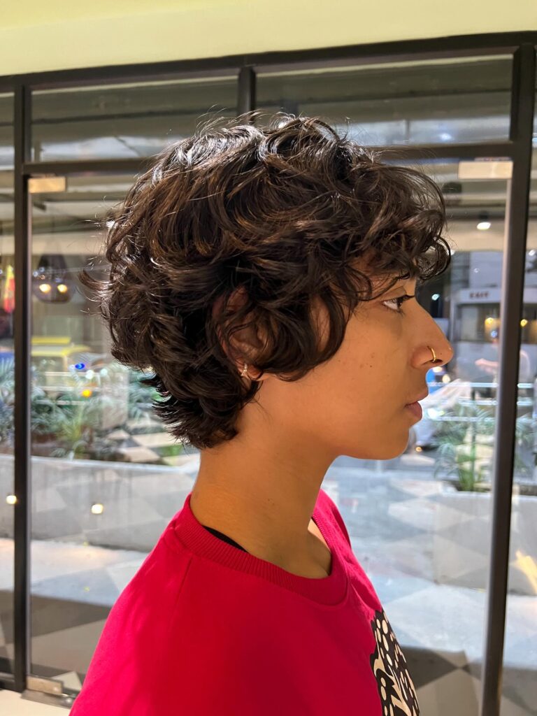 Dark curly pixie haircut with layered volume and soft textured movement.
