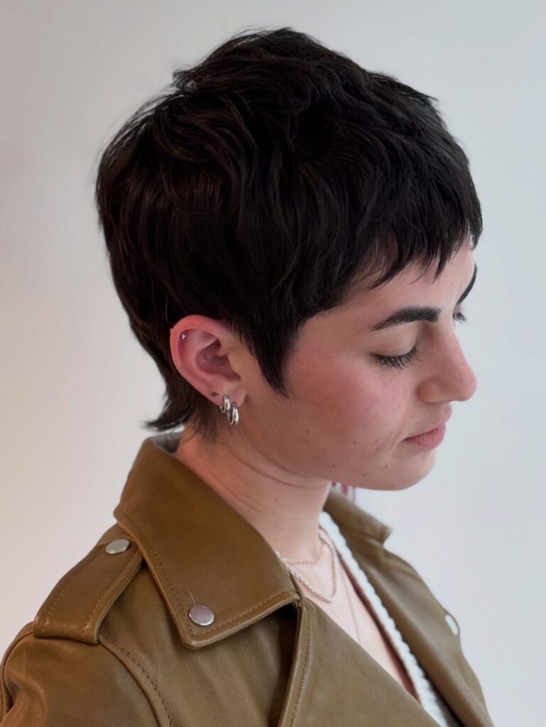 Short brunette pixie haircut with soft textured layers and a wispy fringe.