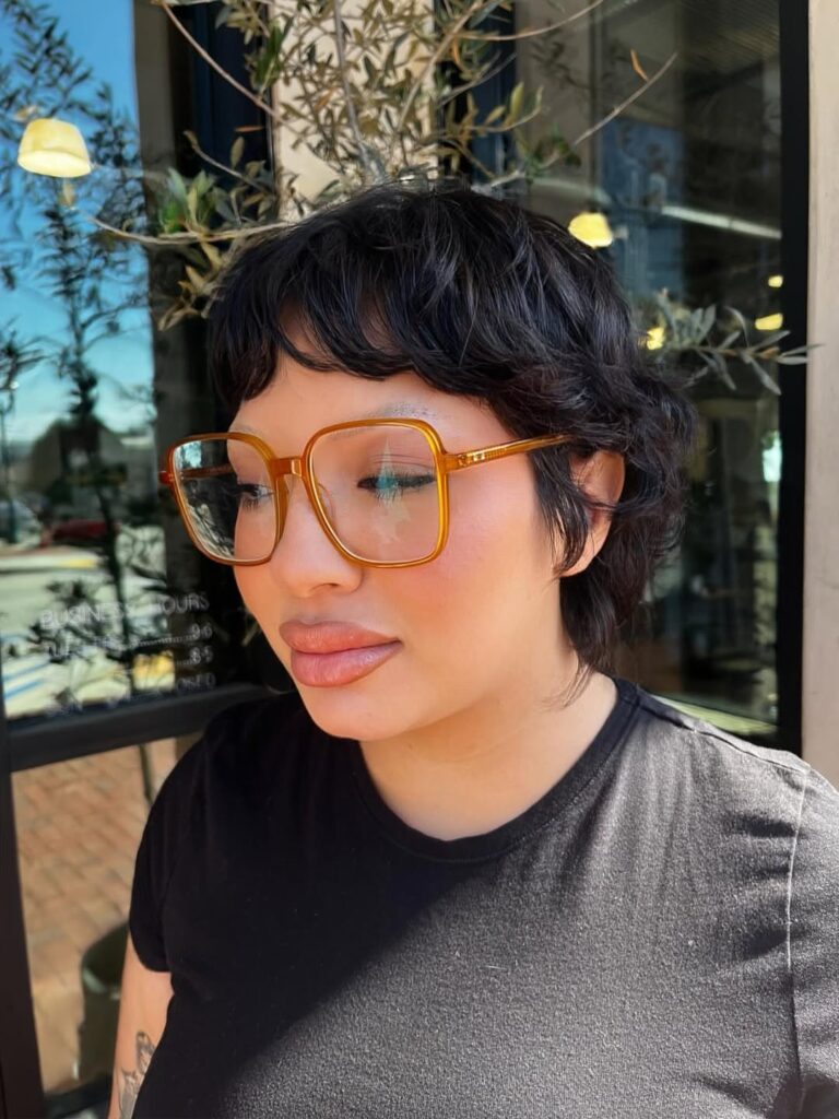 Dark curly pixie bob with soft micro bangs and layered curls around the crown.