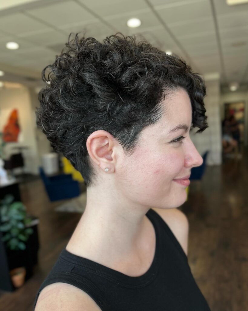 Dark curly pixie undercut with shaved sides and voluminous curls on top.