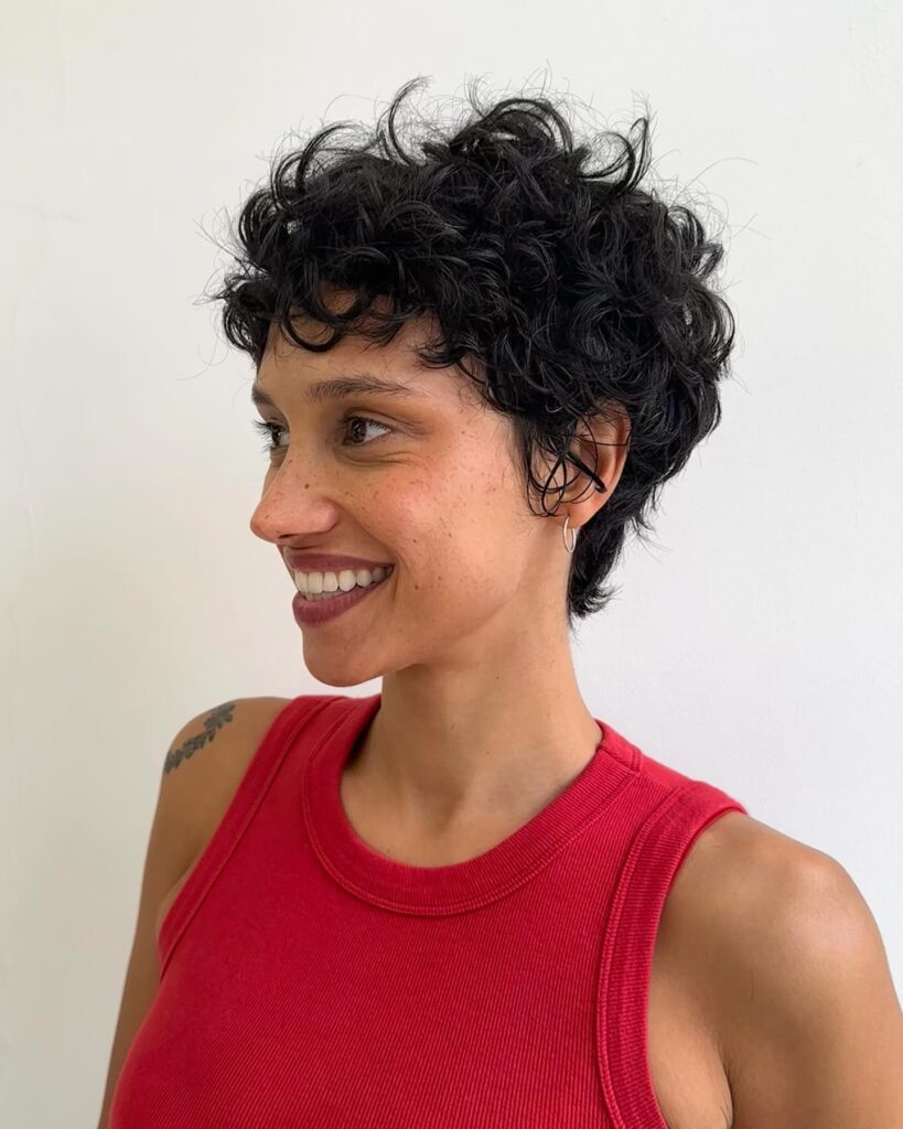 Dark messy curly pixie haircut with soft fringe and layered texture throughout.