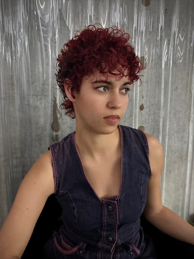 Short cherry red curly pixie haircut with layered curls and cropped sides.