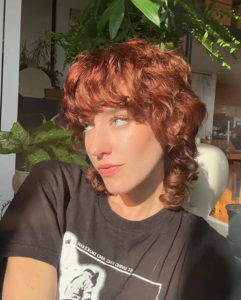 Copper red curly pixie shag with feathered bangs and soft curled layers.