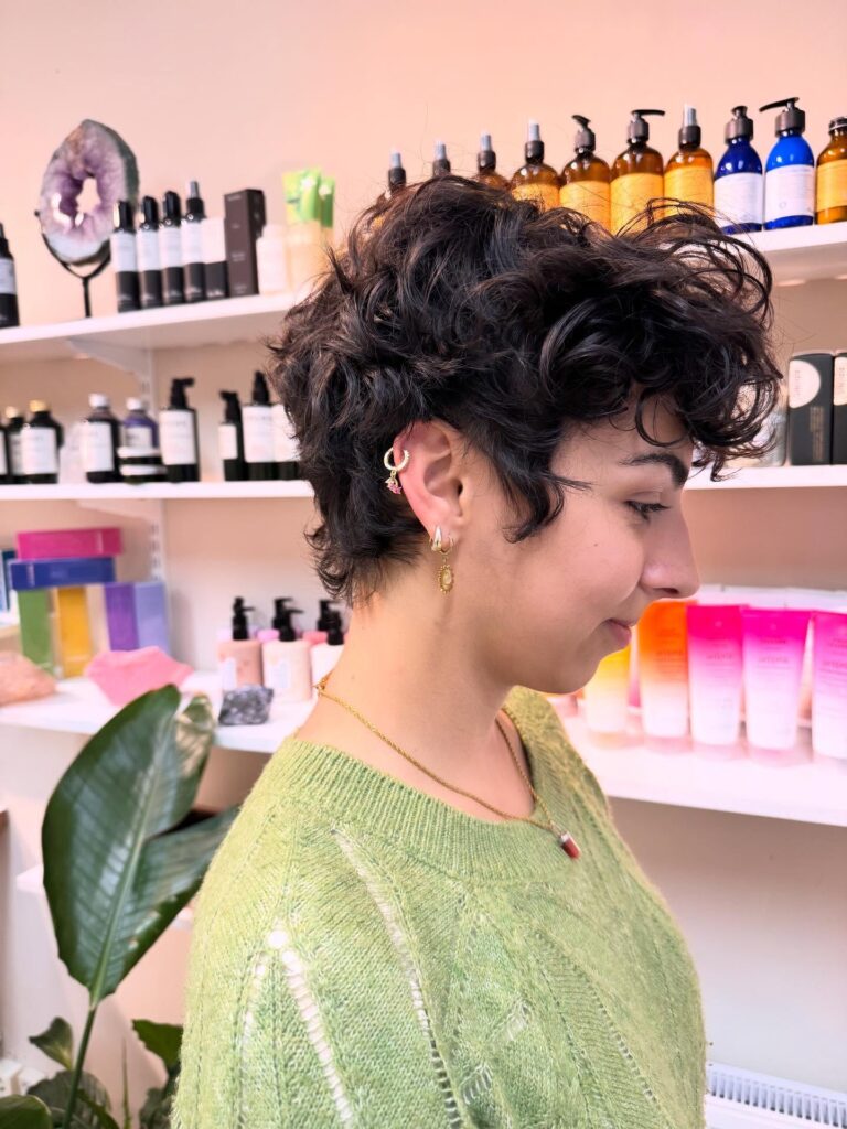 Tousled dark curly pixie haircut with long fringe and soft layered curls.
