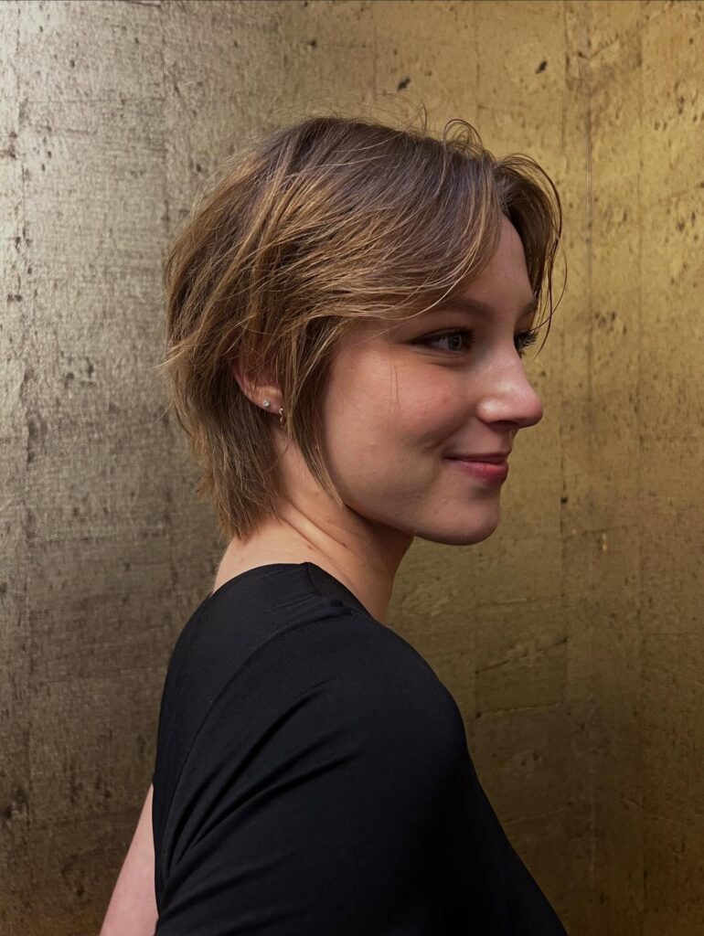 Soft feathered pixie bob with light brown layers and wispy face framing pieces.