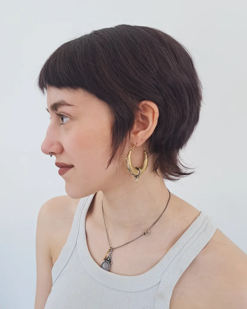 Rounded brunette pixie mullet with short fringe and wispy nape layers.