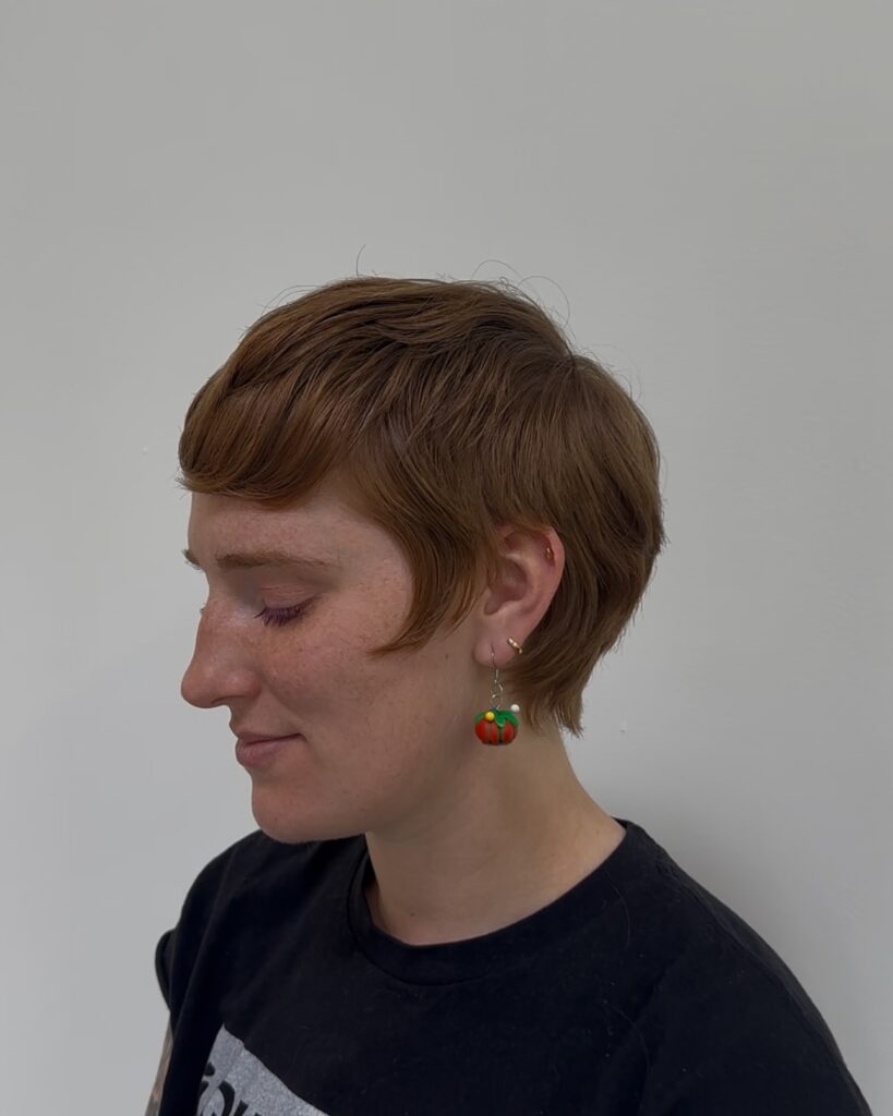 Short ginger pixie haircut with curved fringe and softly tapered layers.