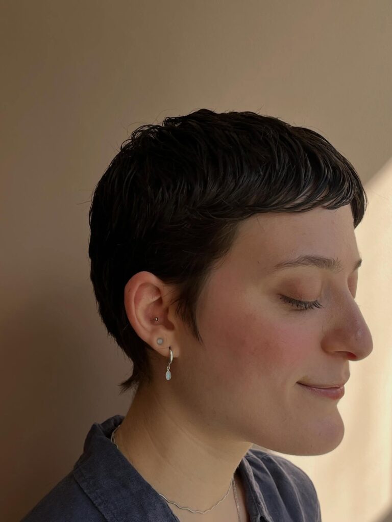 Dark cropped pixie haircut with short micro bangs and softly textured layers.
