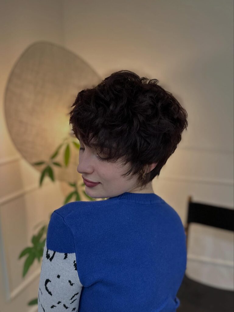 Short curly brunette pixie haircut with fluffy layers and soft textured volume.