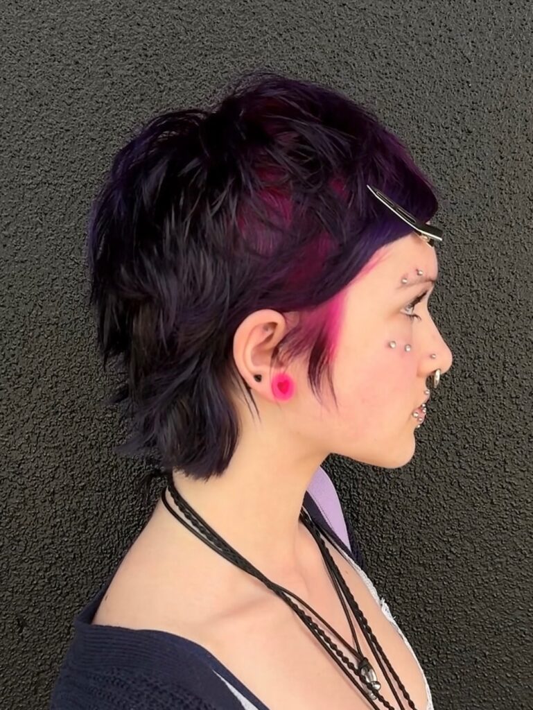 Black pixie mullet haircut with shaggy layers and bright pink and purple peekaboo color.