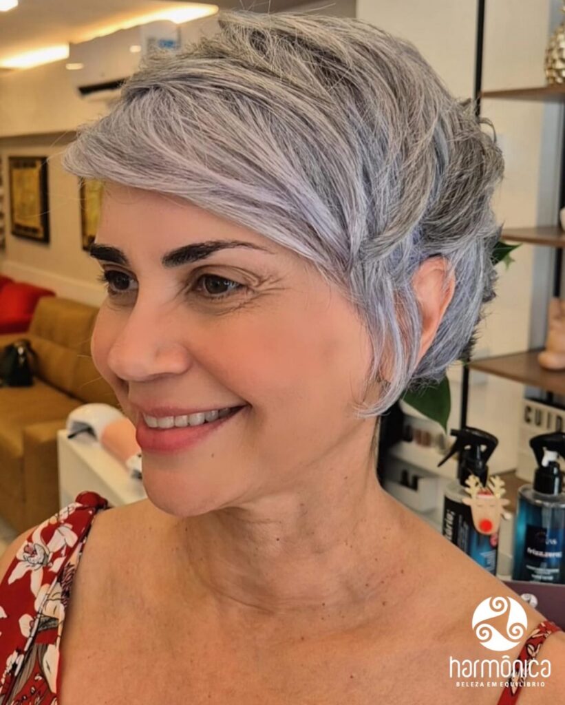 Silver pixie haircut with side swept bangs and softly layered volume through the crown.