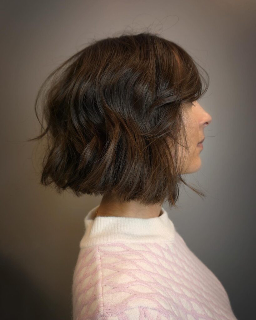 A rounded brunette choppy bob with soft waves and side swept fringe.