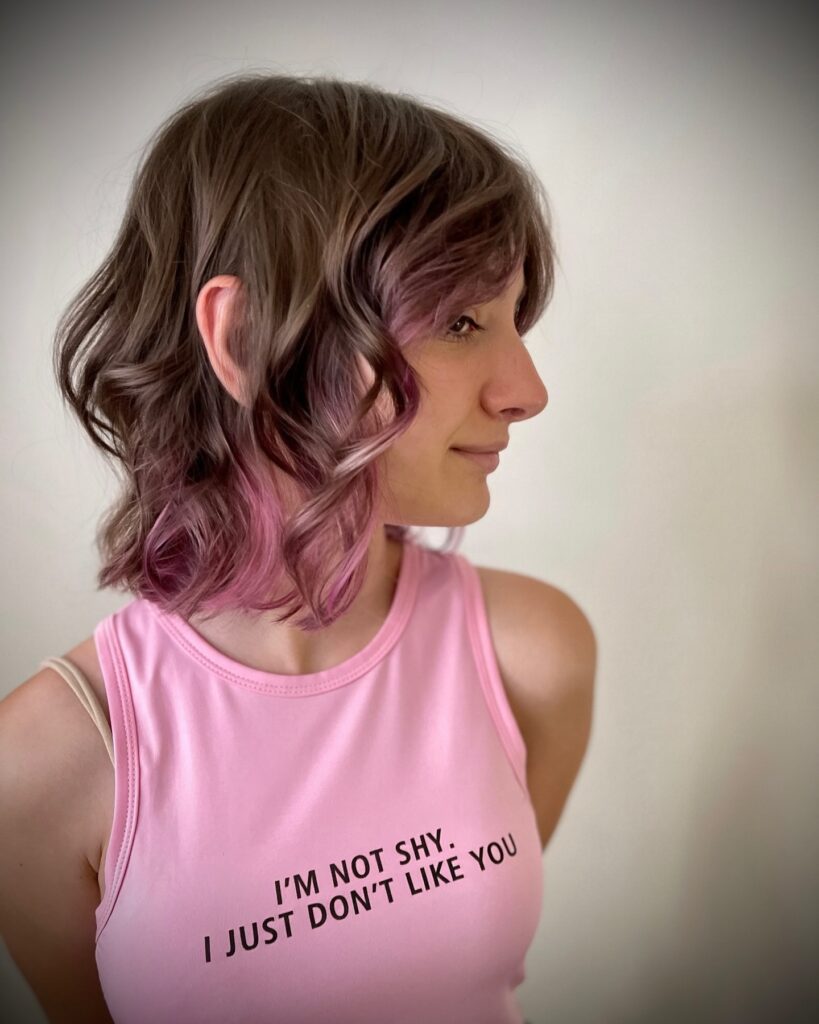 A wavy brunette choppy bob with pink and plum toned highlights.