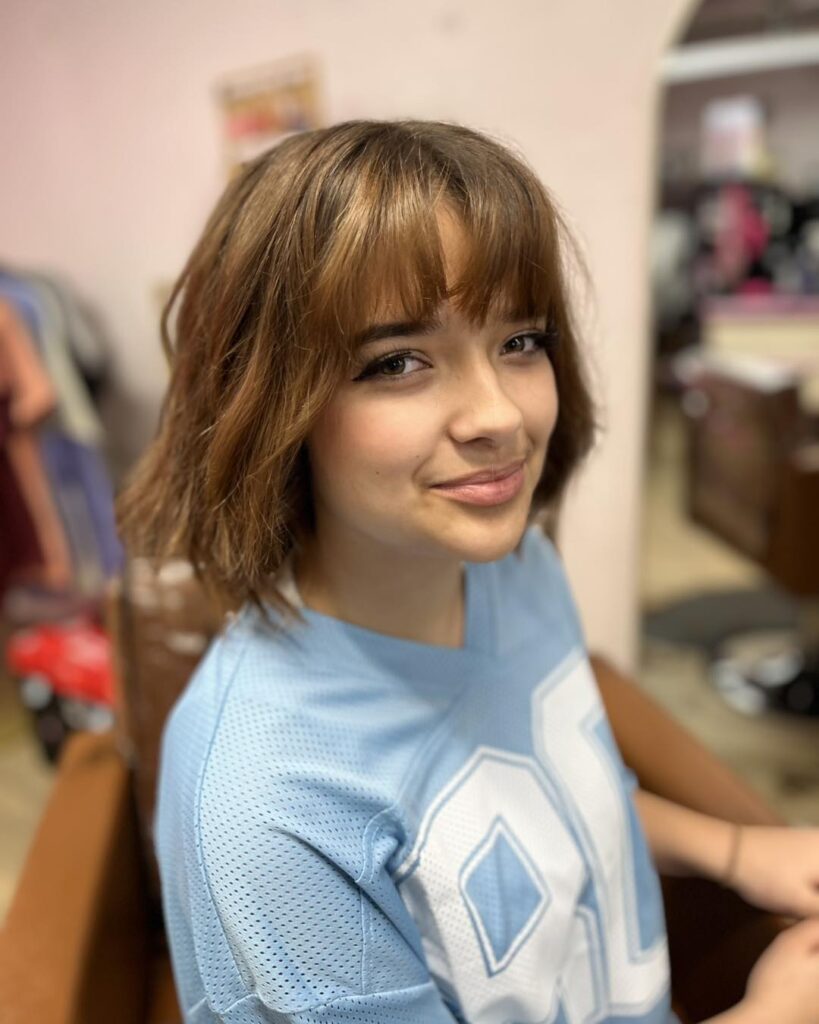 Short layered brunette bob with wispy bangs and soft textured waves around the face.