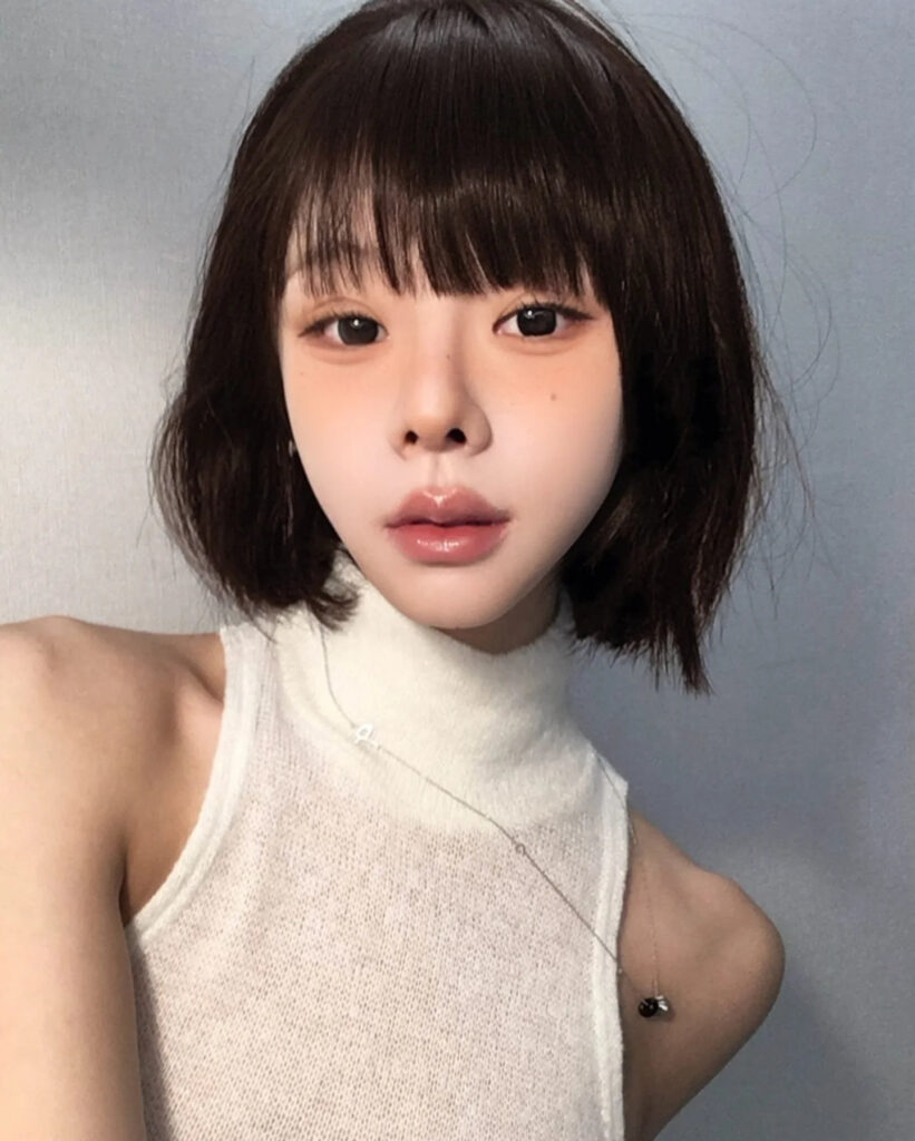 Short dark brown French bob with wispy bangs and textured ends.