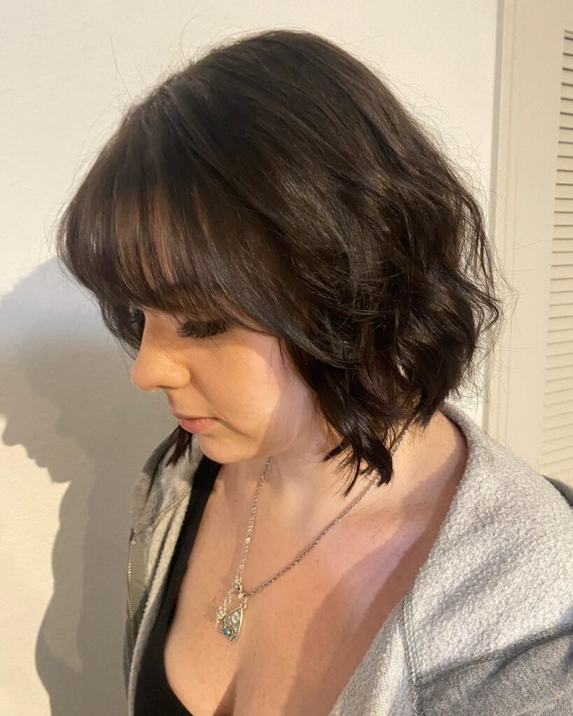 Dark brown layered bob with soft waves and wispy bangs styled with natural bounce.