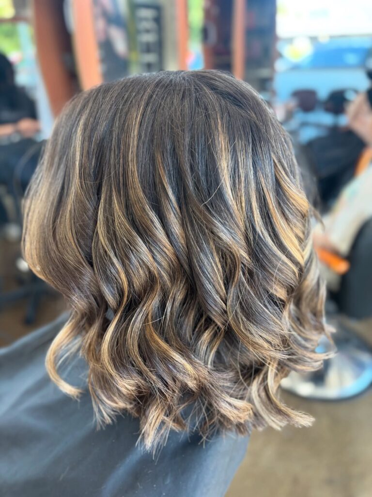 Wavy brunette layered bob with soft honey highlights and loose textured curls.